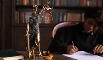 Rechter zit achter tafel met beeld van vrouwe Justitia