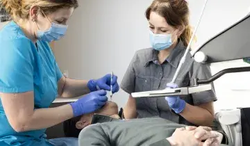 Behandeling bij de tandarts aan de stoel met assistent ernaast